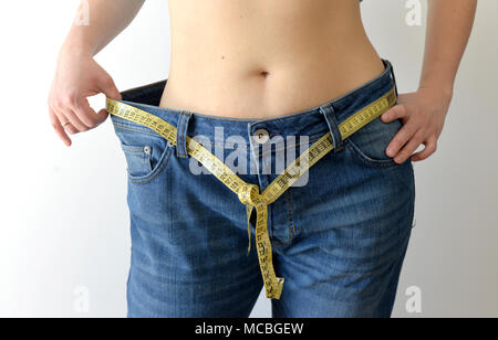 Weight loss concept. Woman shows her weight loss by wearing an old jeans. Healthy lifestyle, dieting concept with oversized jeans. Stock Photo