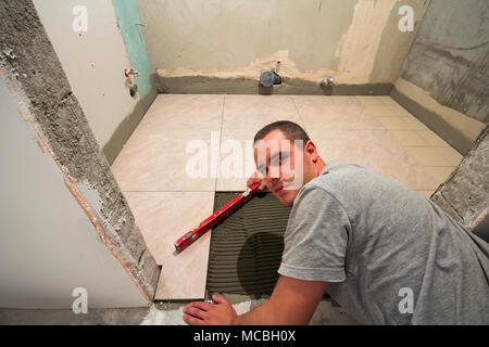 Home tiles improvement - handyman with level laying down tile floor. Renovation and construction concept. Stock Photo