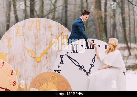 Happy wedding couple softly holding hands at the big vintage clocks in  autumn forest. Creative decorations Stock Photo