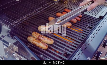 Cooking hot dogs and bratwurst on outdoor gas grill in the Summer. Stock Photo