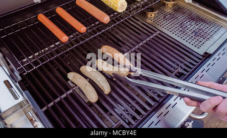Cooking hot dogs and bratwurst on outdoor gas grill in the Summer. Stock Photo