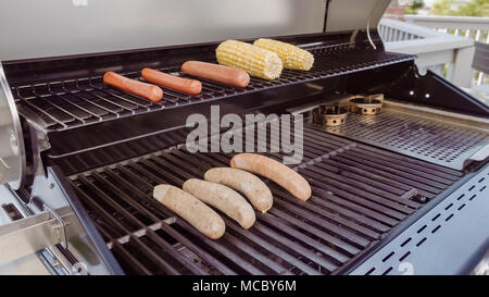 Cooking hot dogs and bratwurst on outdoor gas grill in the Summer. Stock Photo