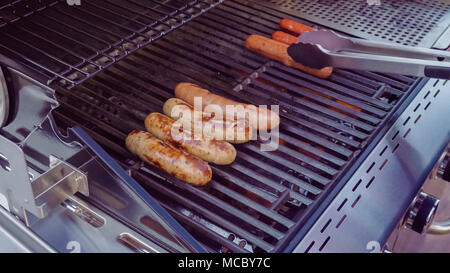 Cooking hot dogs and bratwurst on outdoor gas grill in the Summer. Stock Photo