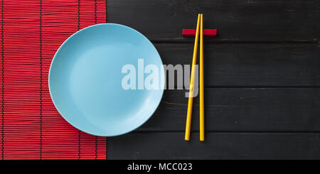 Empty ceramic dish or plate and asian chopsticks on black wooden background Stock Photo
