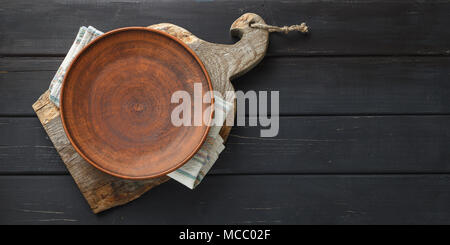 Empty clay dish on rustic cutting board over black wooden background Stock Photo