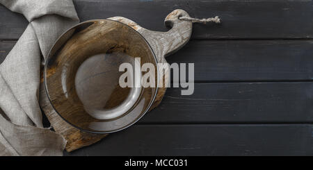 Empty glass dish on rustic cutting board over black wooden background Stock Photo