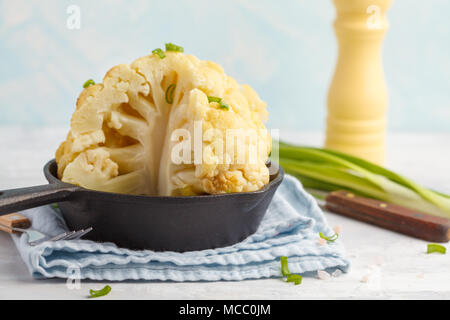 Whole baked cauliflower in a cast-iron frying pan. Healthy vegan food concept. Stock Photo