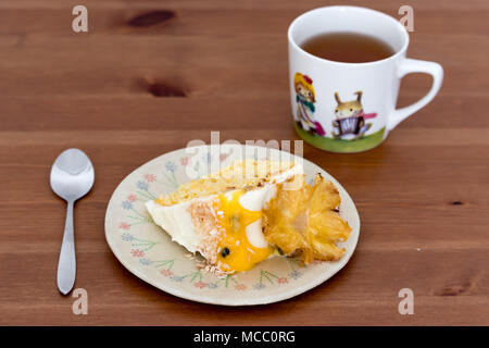 A slice of pineapple and coconut cake with passion fruit curd, served on handmade plate with black tea. Stock Photo