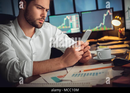 Serious trader using mobile phone app on smartphone for checking stock trading data analysis concept, focused businessman holding cellphone working in