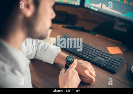 Businessman setting innovative modern smartwatch working on computer in office, young man looking at digital smart watch checking time or using busine Stock Photo