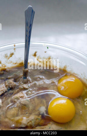 Close up of two raw, broken eggs lying on top batter in a glass bowl with a spoon sticking out of it Stock Photo