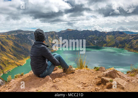 Young female backpacker and tourist looking over the Quilotoa crater lake with turquoise waters along the Quilotoa Loop trekking, Ecuador. Stock Photo