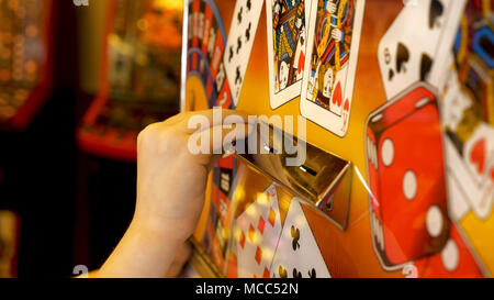 Close-up Of Childs Hands Inserting Coin Into Slots Machine. Stock Photo