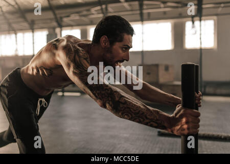 Tough young man pushing sled in cross training gym. Muscular man doing intense physical training at health club. Stock Photo
