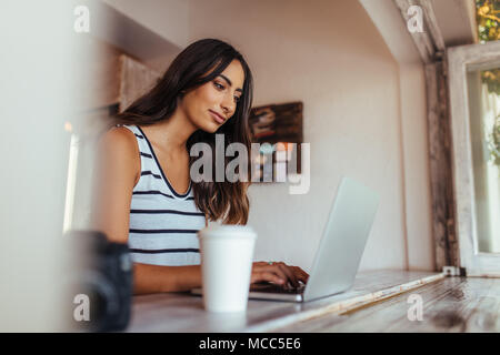 Woman blogger using laptop at home. Woman sitting with coffee glass and camera on the table working on her laptop computer. Stock Photo