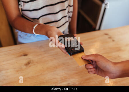 Woman entrepreneur using a wireless point of sale machine to effect a cashless payment. Close up of a woman holding a wireless point of sale machine w Stock Photo