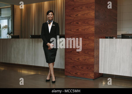 Full length portrait of female hotel receptionist standing at workplace. Beautiful woman receptionist working in hotel. Stock Photo