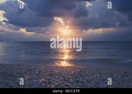 Evening sunset on the sea,. purple cloud in orange sky. small sun look far away and getting dark. Light evening light. Clean clear water. Cloudy sky.  Stock Photo