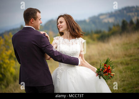 Loving couple are newlyweds in the mountains. Stylish bride with a bouquet kisses the groom. love, fidelity and shadowing concept. Mountain Stock Photo