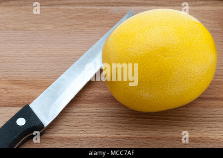 knife and yellow fresh lemon close-up on a wooden cutting board. Stock Photo