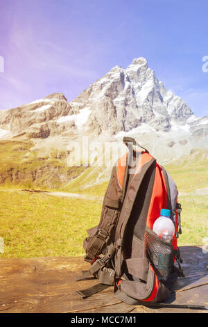 Hipster red and black backpack and bottle on the table with sunlight in the morning and mountain background, Tourist backpack bag is located on wooden Stock Photo