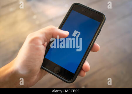 Bangkok, Thailand - March 17, 2018 : iPhone 7 held in one hand showing its screen with Facebook logo. Stock Photo