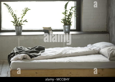 Unmade messy double bed for two with crumpled bedding sheet linen near window in modern comfortable bedroom grey interior design with nobody, empty co Stock Photo