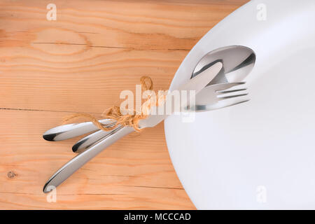 Place setting. Tied with rough rope cutlery on white plate. On wooden table background Stock Photo