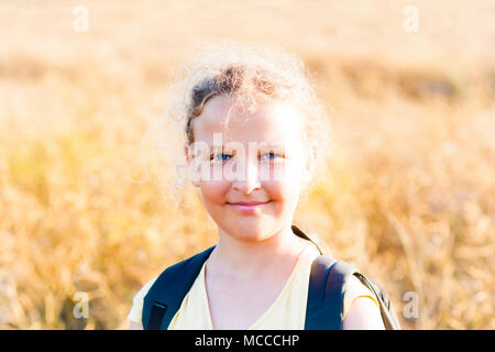 Summer girl with rucksack on sunset background meadow. Stock Photo