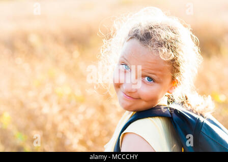 Summer girl with rucksack on sunset background meadow. Stock Photo