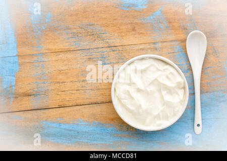 live organic Greek yogurt in a white ceramic bowl against grunge wood, top view Stock Photo