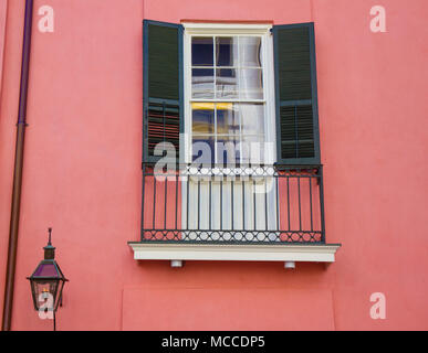 Window with with green shutters on salmon colored house in the French Quarter, New Orleans, Louisiana. Small cast iron balcony below window, gas lamp Stock Photo