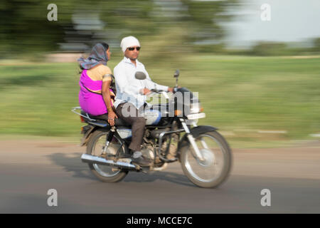 A woman in a spree sitting side saddle as a passenger on a speeding motorbike in India Stock Photo