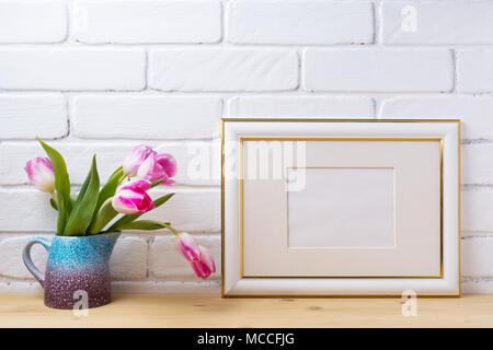Gold decorated landscape, frame mockup with magenta pink tulip in the purple blue pitcher vase. Empty frame mock up for presentation artwork. Template Stock Photo
