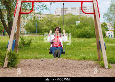pacified woman riding on a swing on a cloudy summer day in the city Stock Photo