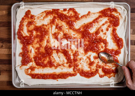Man spreading tomato sauce on rolled out dough for homemade pizza Stock Photo