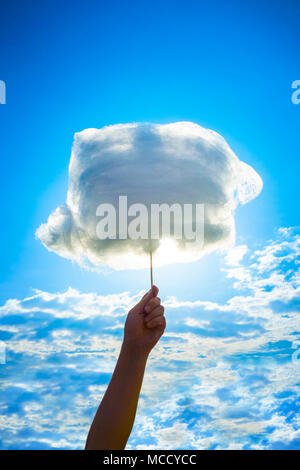 Holding Sweet Cotton Candy on Stick on Blue Cloudy Sky Background. Stock Photo