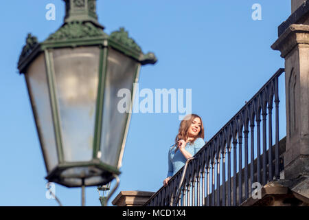 Prague - April 10: Beautiful young woman, tourist walks on the brick, she stands and poses behind the balustrade of Charles Bridge nearby Prague Castl Stock Photo