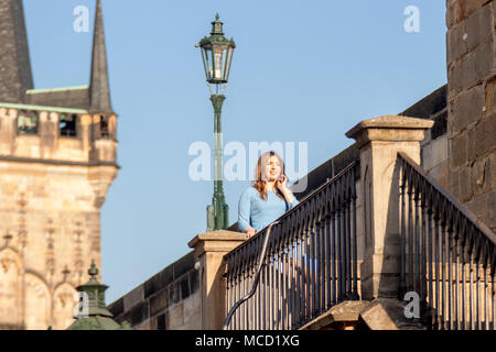 Prague - April 10: Beautiful young woman, tourist walks on the brick, she stands and poses behind the balustrade of Charles Bridge nearby Prague Castl Stock Photo