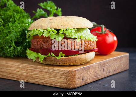 Fresh vegan Burger with tomato, cucumber, lettuce and vegan cutlet on wooden Board. Stock Photo