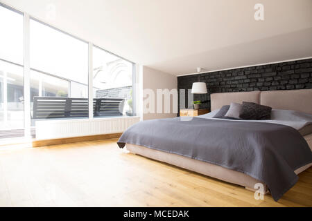 Grey bedding on bed in bright bedroom interior with windows and wooden floor Stock Photo
