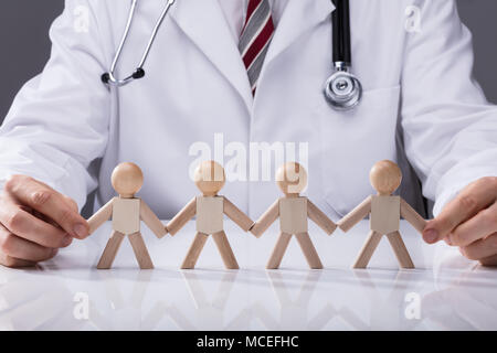 Close-up Of Doctor Holding Hand Of Wooden Figures Standing In A Row Stock Photo