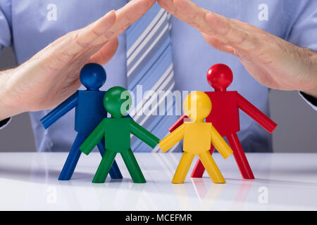 Close-up Of A Human Hand Protecting Multi Colored Human Figures On White Desk Stock Photo