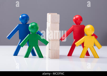 Close-up Of Multi Colored Human Figures Separated By Stacked Wooden Blocks Against Grey Background Stock Photo