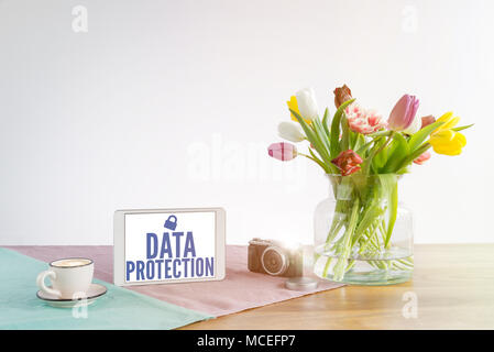 Data protection written on tablet screen for security and safety reasons in business concerning the gdpr on wooden office desk with flowers in front o Stock Photo