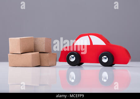 Red Car And Cardboard Boxes On White Desk Against Grey Background Stock Photo
