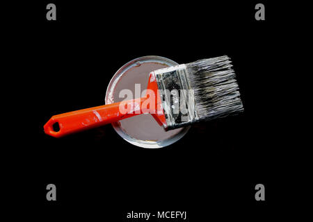 Used paintbrush with an orange handle, placed on top of a white paint can with a dark background and seen from above. Stock Photo