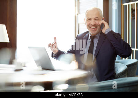 Middle-aged Caucasian male entrepreneur talking on smartphone with colleague and smiling happily Stock Photo