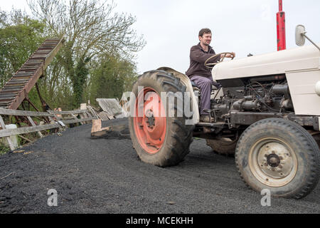 Vintage John Deere tractor having been restored being driven by a young farmer in a livery yard to plough out the crushed tires used as a horse yard. Stock Photo