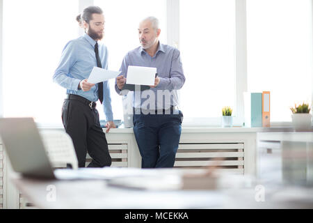 Two businessmen with documents standing at office and discussing new plans Stock Photo